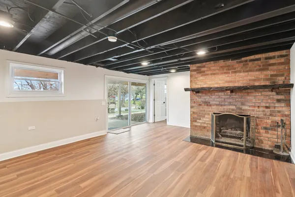 a view of an empty room with wooden floor fireplace and a window