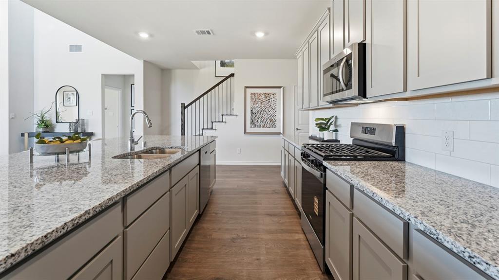 4197 Waldron Trail Forney, TX 75126 - Photo 4 of 25 Kitchen featuring light-toned cabinetry, stainless steel appliances, a subway tile backsplash, granite countertops, and wood-finish flooring