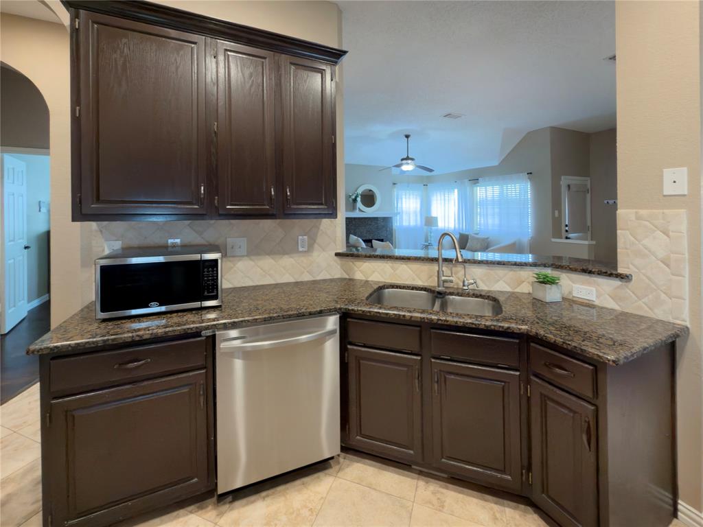 4234 Timberglen Road Dallas, TX 75287 - Photo 8 of 32 Kitchen featuring granite countertops, dark wood cabinetry, a stainless steel dishwasher, a double basin sink with a gooseneck faucet, and a tiled backsplash