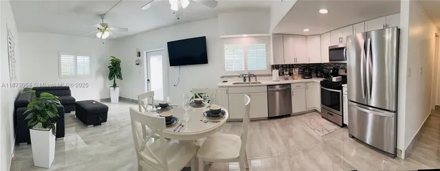 a kitchen with stainless steel appliances a microwave a stove a sink dishwasher a refrigerator with a dining table and chairs with wooden floor