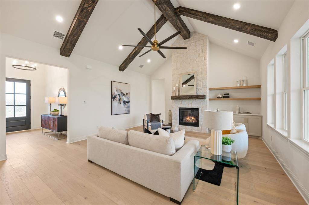 3006 Wheeler Branch Road Granbury, TX 76049 - Photo 8 of 29 Vaulted ceilings with exposed wood beams, a stone-clad fireplace with wood mantle, light wood-finish flooring, multiple windows, and open shelves