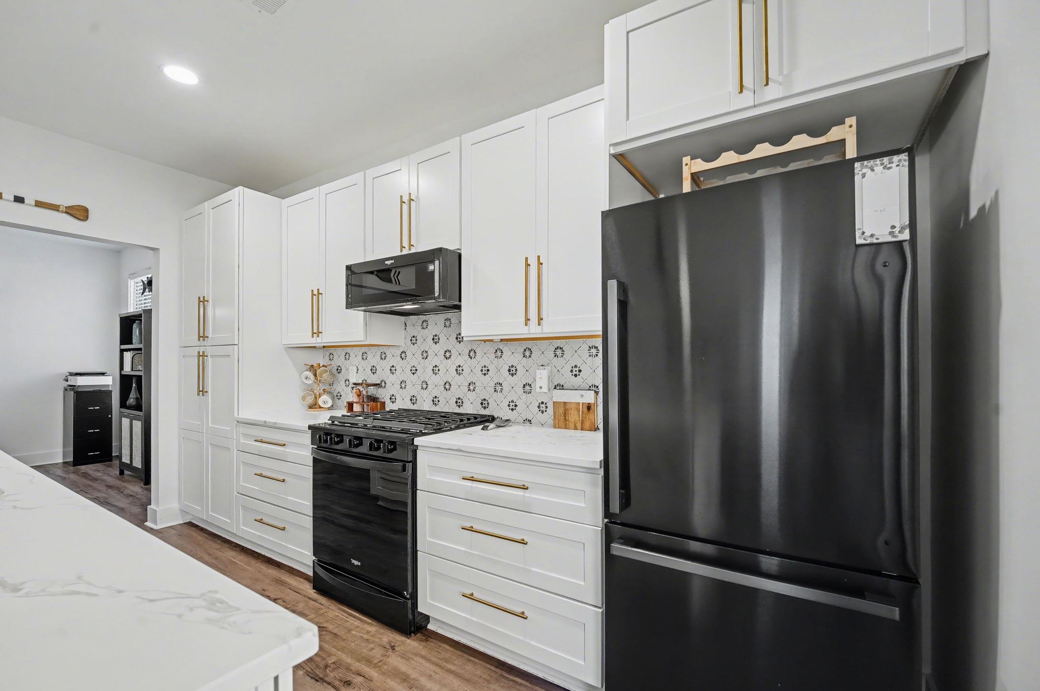236 Brown Pelican Loop Pawleys Island, SC 29585 - Photo 19 of 38 Kitchen with black appliances, white cabinets, light wood-style flooring, backsplash, and light stone countertops