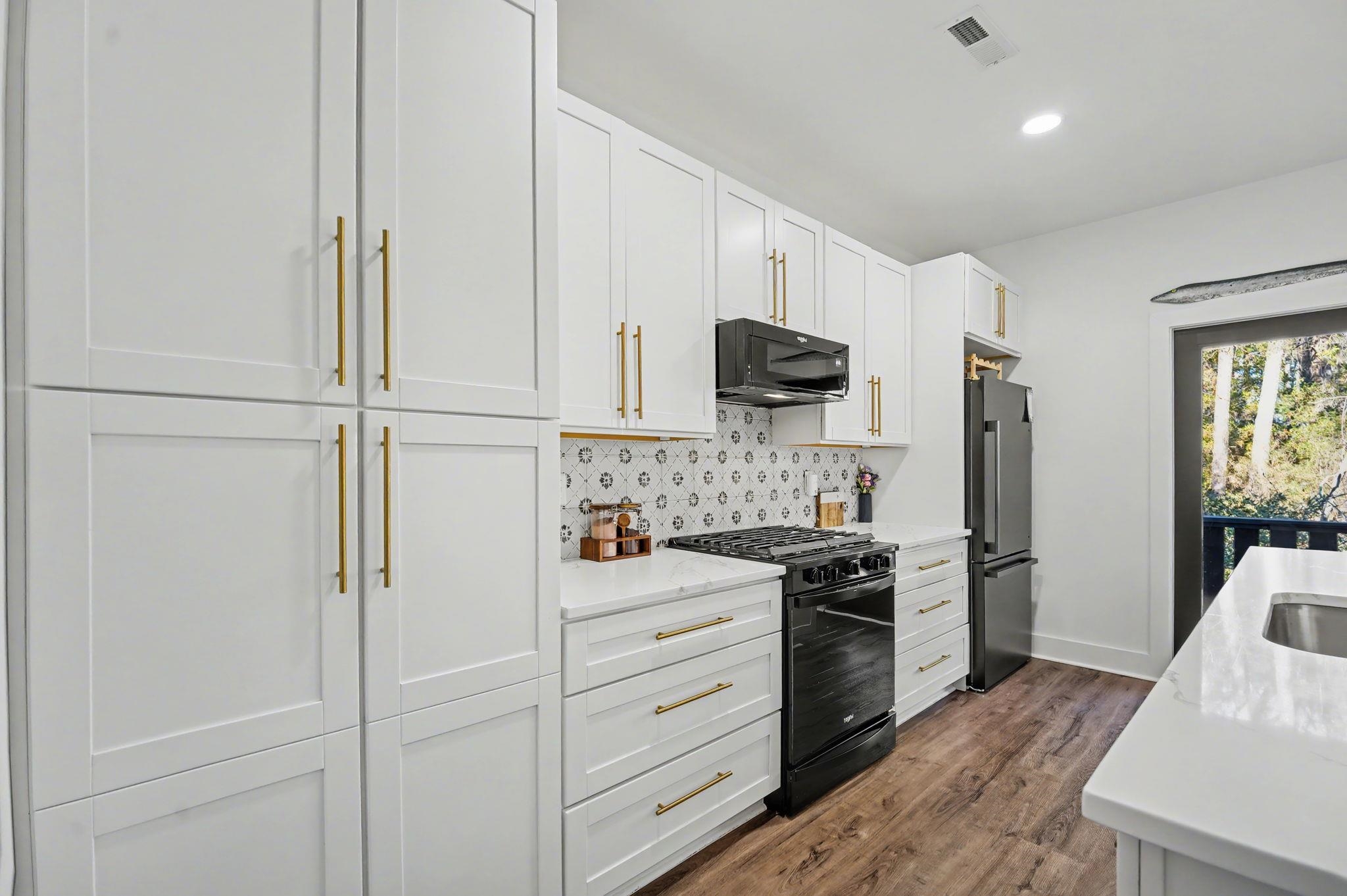 236 Brown Pelican Loop Pawleys Island, SC 29585 - Photo 20 of 38 Kitchen with white cabinets, black appliances, light stone counters, backsplash, and dark wood finished floors