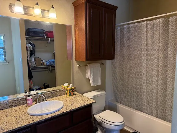 a bathroom with a granite countertop sink a toilet a mirror and shower curtain