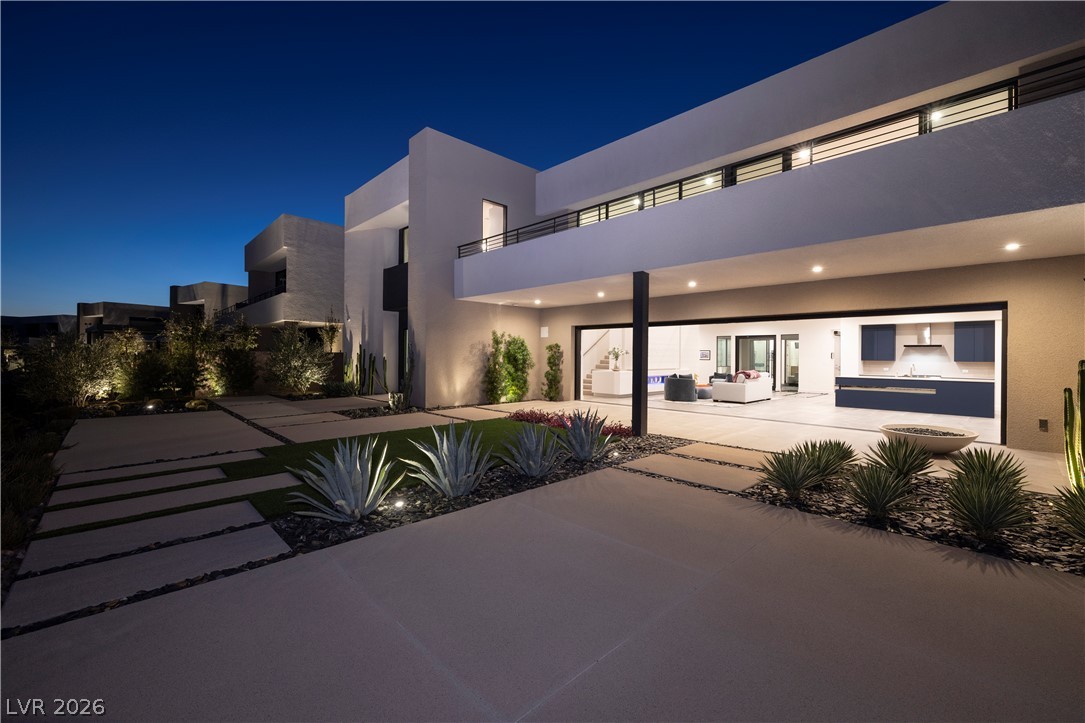 25 Falling Ridge Lane Henderson, NV 89011 - Photo 15 of 48 Modern architecture glows at twilight, featuring an illuminated patio with an open-concept indoor-outdoor kitchen and living space.