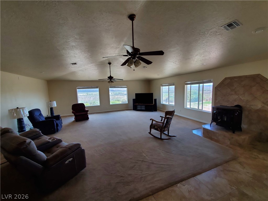 5272 Truman Lane Caliente, NV 89008 - Photo 6 of 43 Carpeted living room featuring a wood stove, a textured ceiling, baseboards, and a ceiling fan