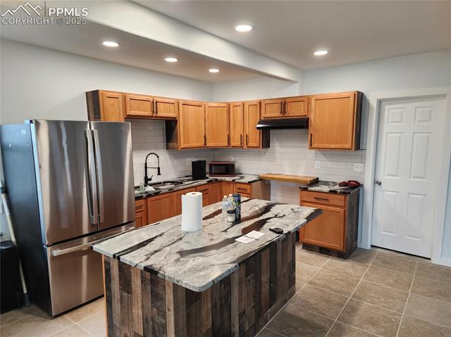 32174 Torrence Road Yoder, CO 80864 - Photo 5 of 13 Kitchen featuring a sink, stone countertops, freestanding refrigerator, under cabinet range hood, and backsplash