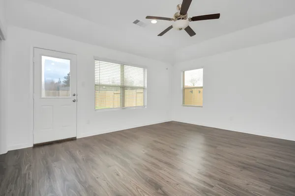 an empty room with wooden floor ceiling fan and windows