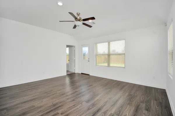 an empty room with wooden floor fan and windows