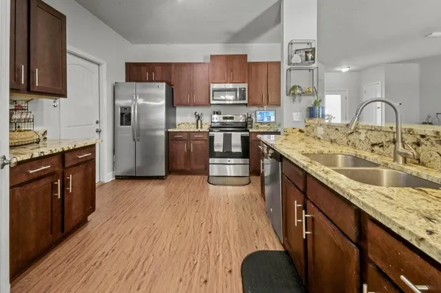 a kitchen with stainless steel appliances granite countertop a refrigerator a sink dishwasher a stove with wooden floor and cabinets