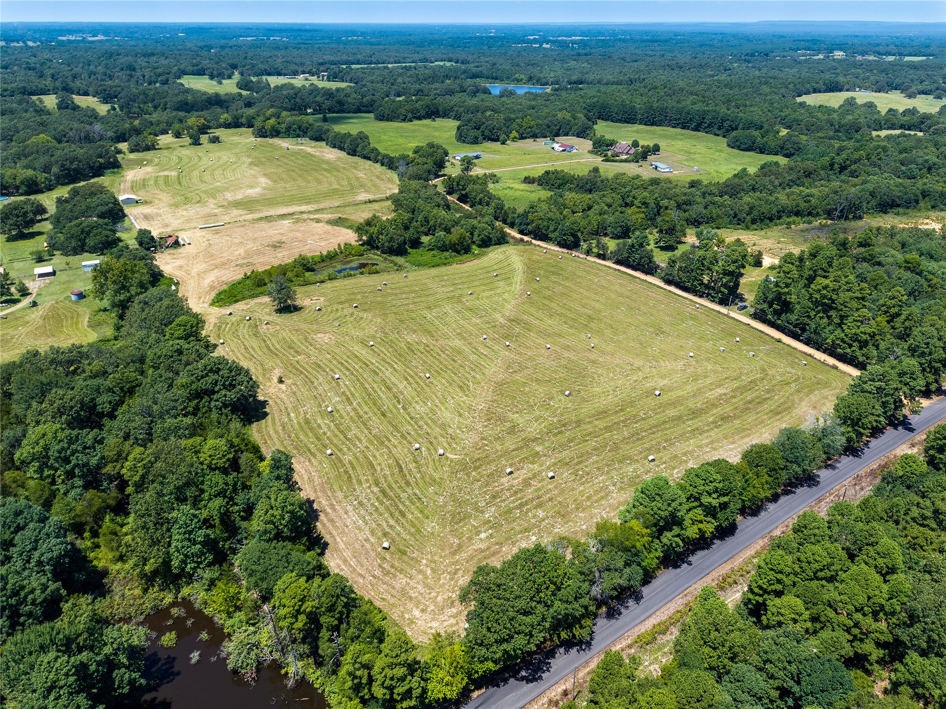 Expansive acreage featuring multiple fields, wooded borders, a paved road frontage, and a visible pond