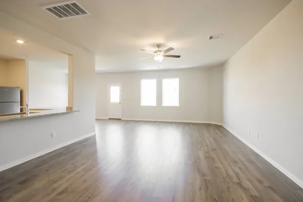 a view of an empty room with wooden floor and a ceiling fan
