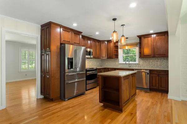 a kitchen with kitchen island granite countertop wooden floors stainless steel appliances a sink and a window