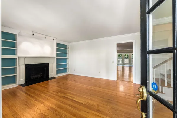 a view of an empty room with wooden floor fireplace and a window