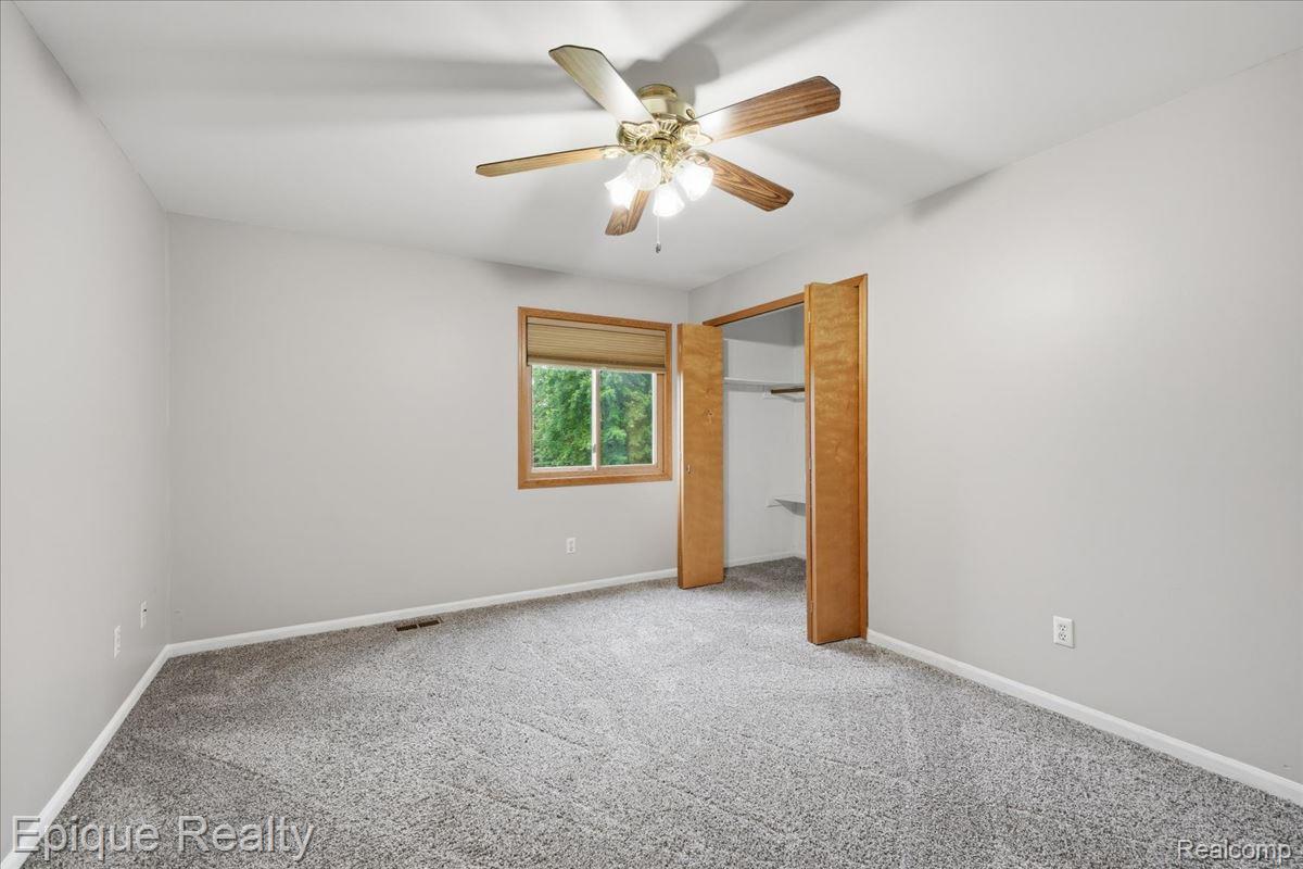 1221 Rhodes Road Lake Orion, MI 48360 - Photo 38 of 72 Spacious room featuring neutral carpeting, light gray walls, a ceiling fan with integrated lighting, a window with wood trim, and a bi-fold door closet with built-in shelving