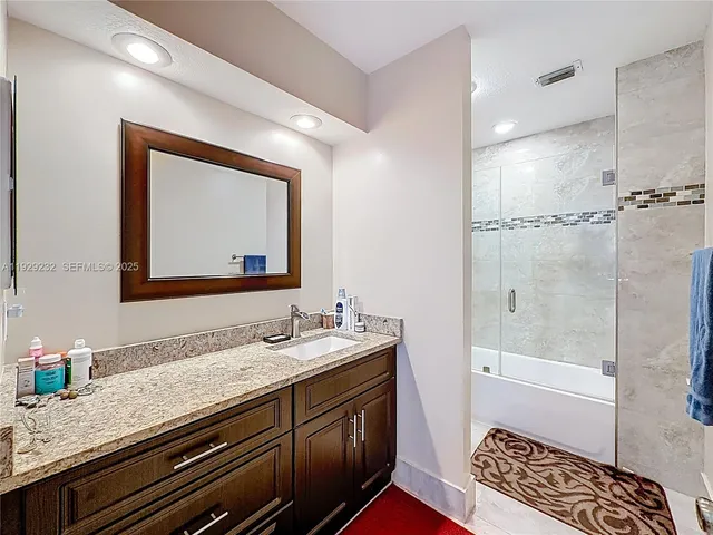 a bathroom with a granite countertop double vanity sink a mirror and a shower