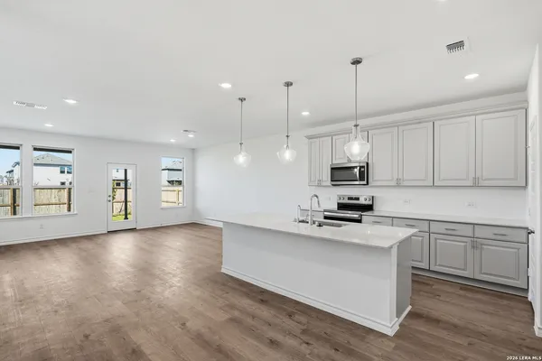a kitchen with granite countertop a stove a sink and white cabinets with wooden floor