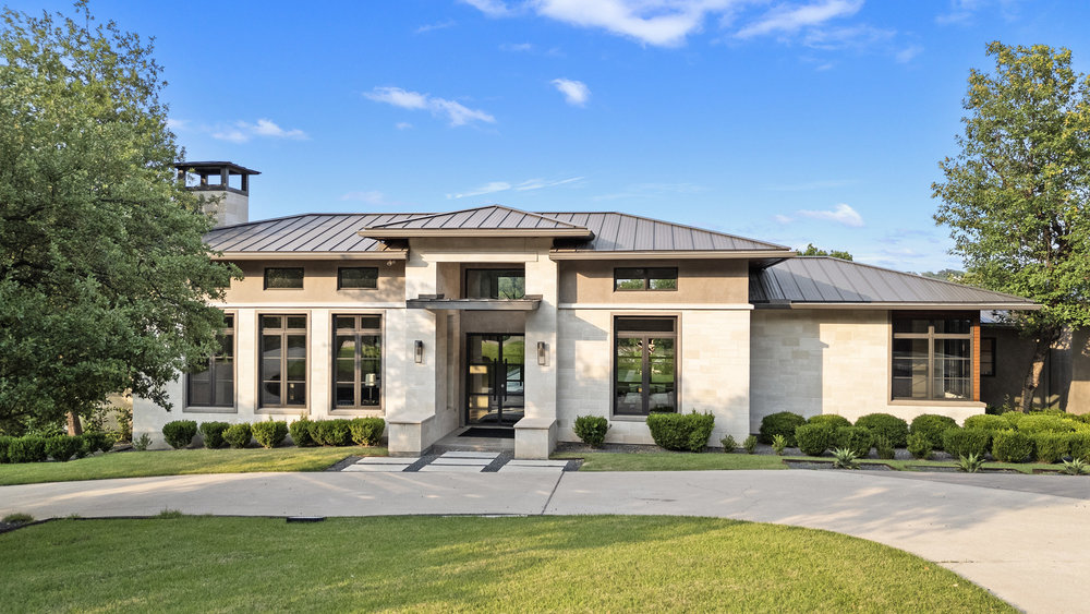 1905 Paisano Road Austin, TX 78746 - Photo 2 of 40 A striking contemporary residence featuring a blend of stone and stucco, set against a vibrant green lawn.