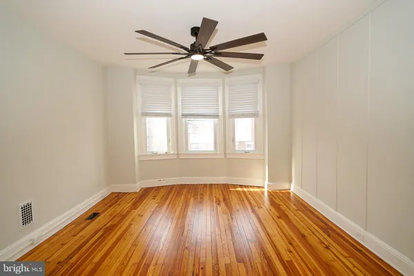 an empty room with wooden floor fan and windows