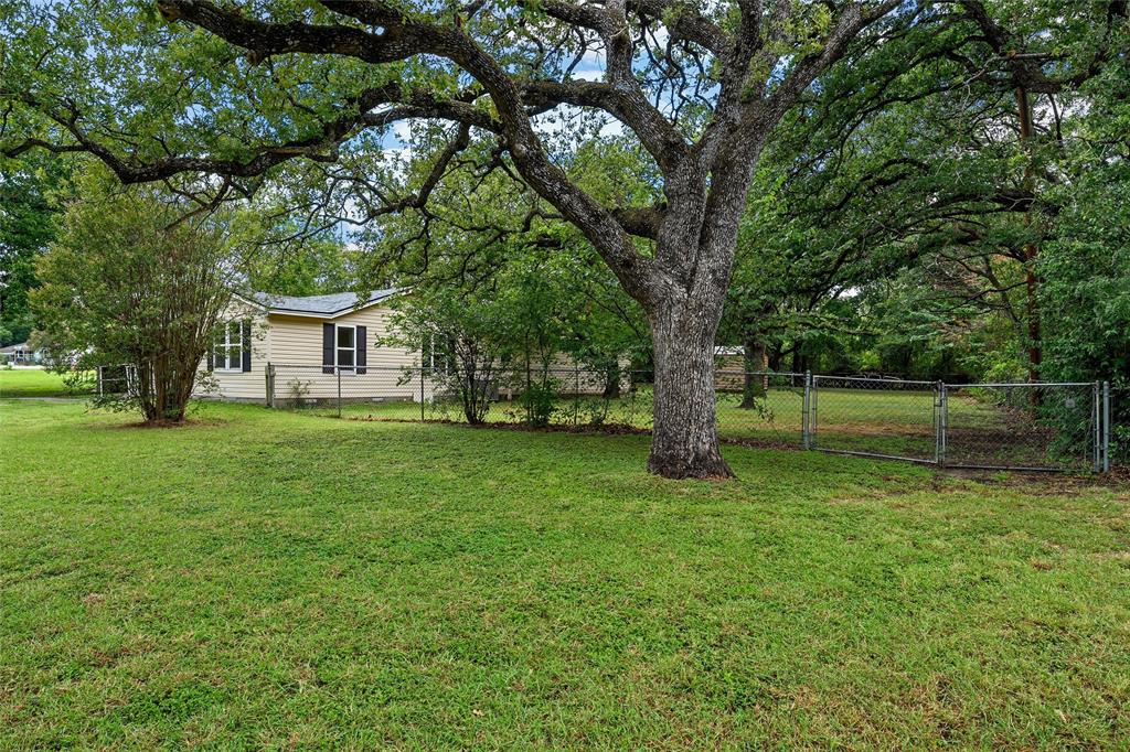 4704 Williams Road Bellmead, TX 76705 - Photo 23 of 32 Expansive green lawn with mature shade trees, chain-link fencing, and a light-colored exterior dwelling with dark shutters