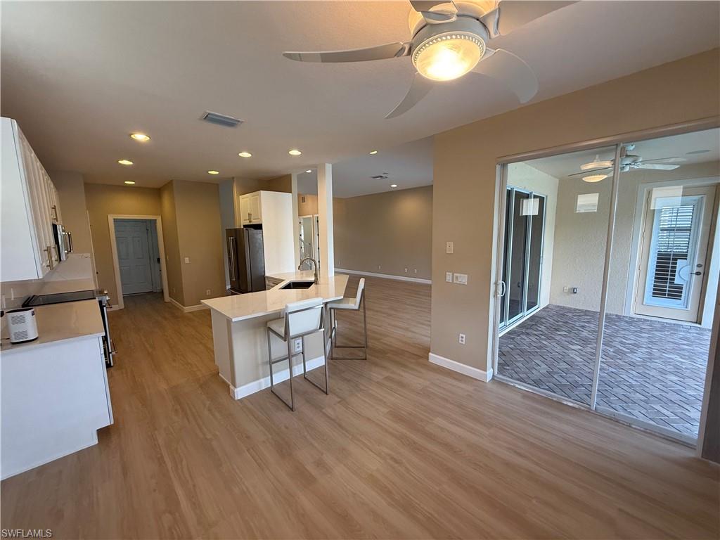 10228 Cobble Hill Road Bonita Springs, FL 34135 - Photo 30 of 31 Kitchen with white cabinets, light stone counters, a kitchen bar, open floor plan, and appliances with stainless steel finishes
