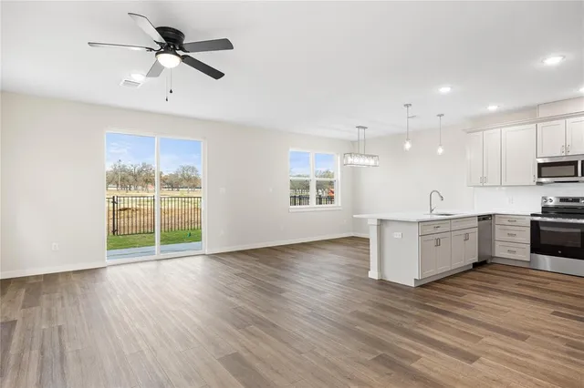 a view of an empty room with wooden floor and a kitchen