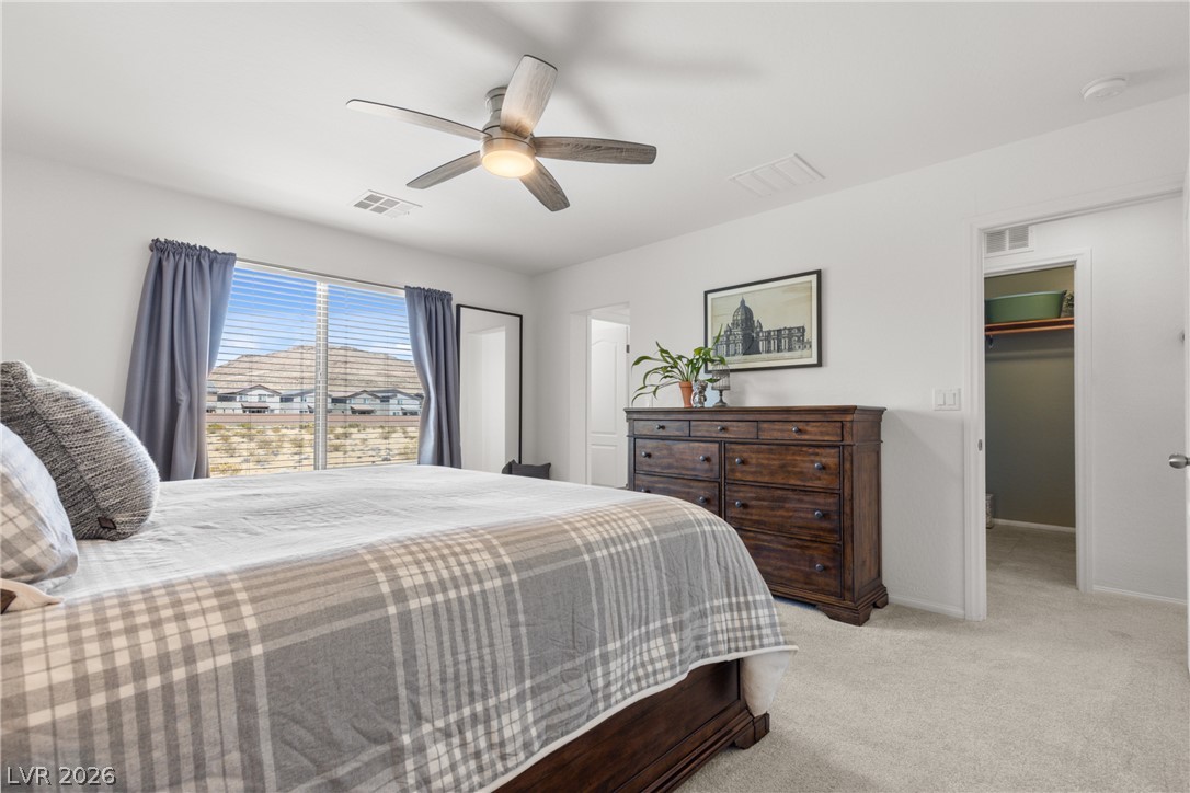 891 Earth Luster Road Las Vegas, NV 89178 - Photo 13 of 48 A well-lit bedroom features plush carpeting and a modern ceiling fan, offering a pleasant and relaxing retreat.