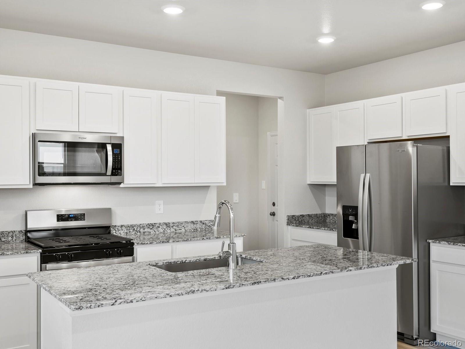 4684 Rabbitbrush Street Johnstown, CO 80534 - Photo 17 of 45 a kitchen with granite countertop a sink a stove a microwave a refrigerator and white cabinets