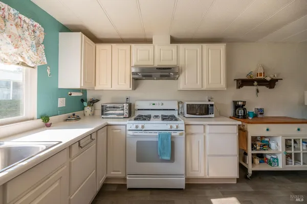 a kitchen with a sink dishwasher a stove and white cabinets with wooden floor