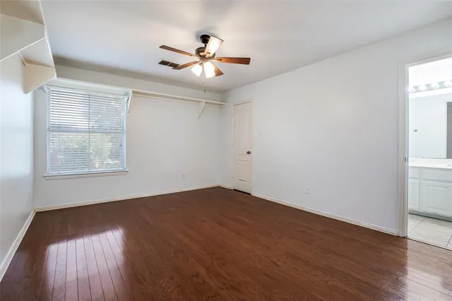 an empty room with wooden floor chandelier fan and windows
