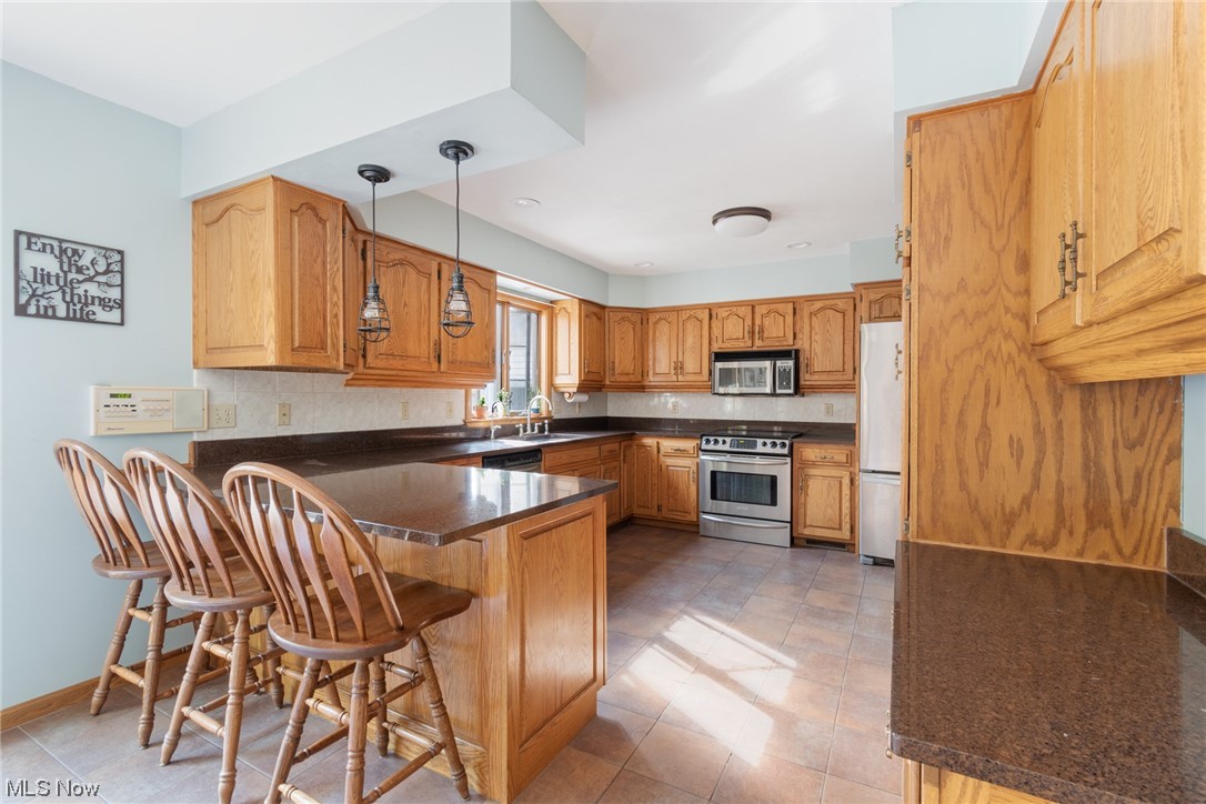 8089 Thomas Road Lisbon, OH 44432 - Photo 20 of 46 Kitchen featuring kitchen peninsula, light tile floors, stainless steel appliances, a breakfast bar, and decorative light fixtures