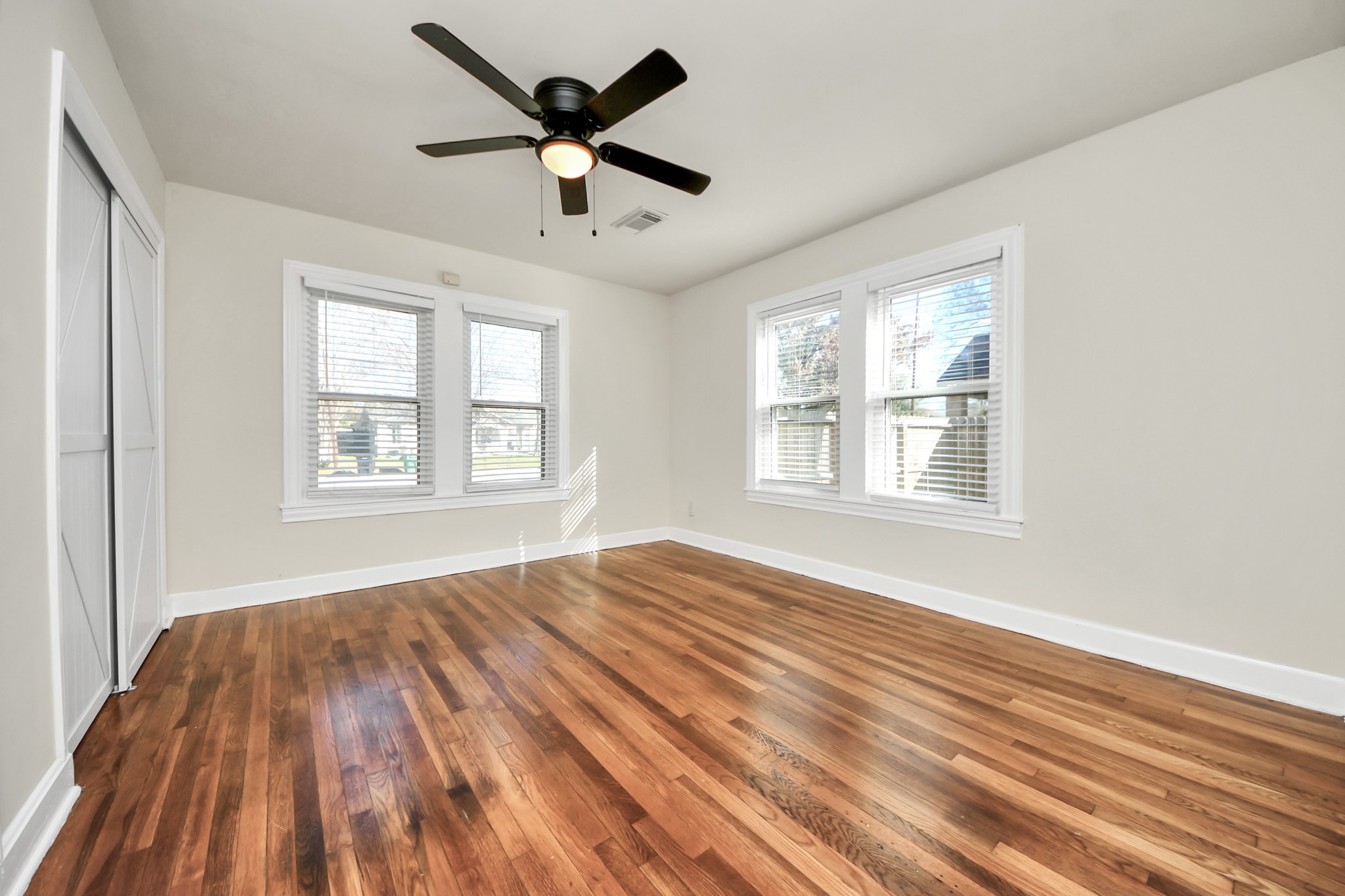 516 Eleanor Street Houston, TX 77009 - Photo 14 of 25 Light-filled primary bedroom with wood flooring, soft neutral tones, a ceiling fan, large windows, and spacious closets for comfortable living.