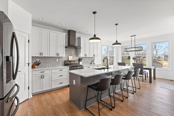 a kitchen with stainless steel appliances granite countertop a stove a sink a refrigerator a dining table and chairs with wooden floor