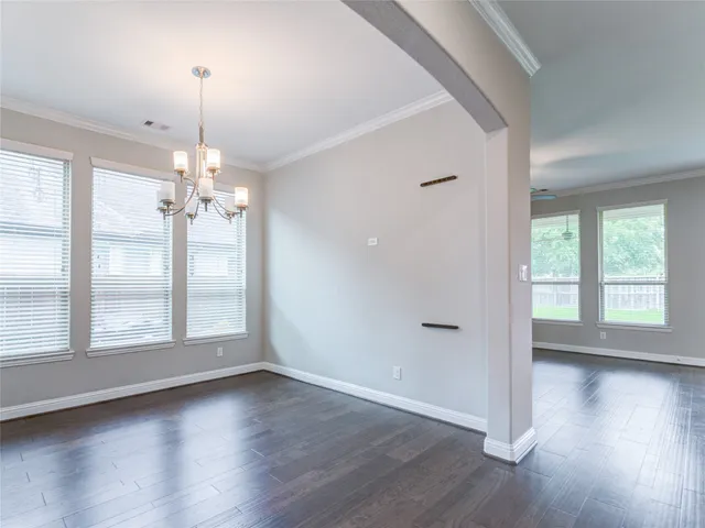 a view of an empty room and kitchen with wooden floor