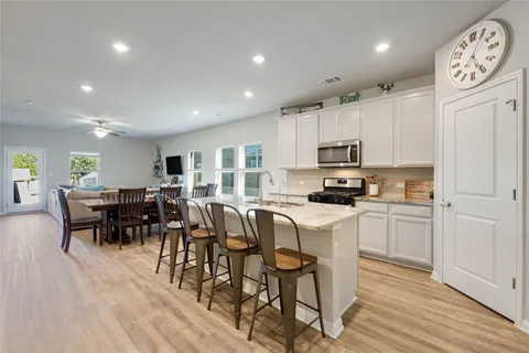 a kitchen with stainless steel appliances granite countertop a refrigerator a stove top oven a dining table and chairs with wooden floor