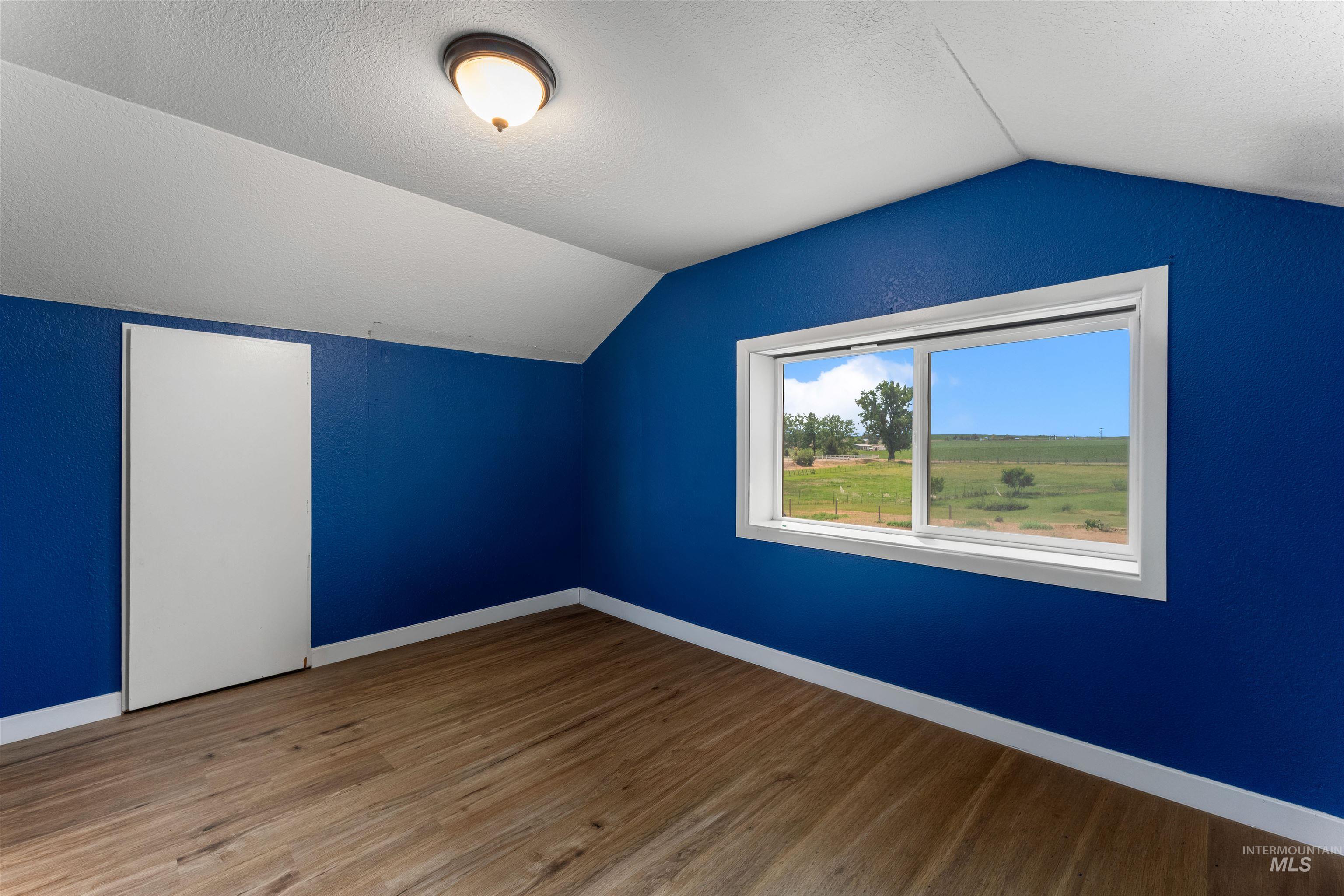 17441 Upper Pleasant Ridge Road Caldwell, ID 83607 - Photo 17 of 40 Attic room featuring wood-finish flooring, a white trim window, a ceiling-mounted light fixture, and a built-in storage door