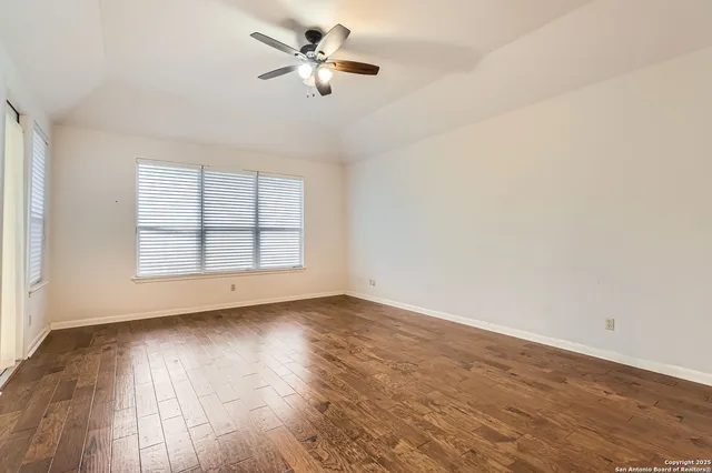 an empty room with wooden floor chandelier fan and windows
