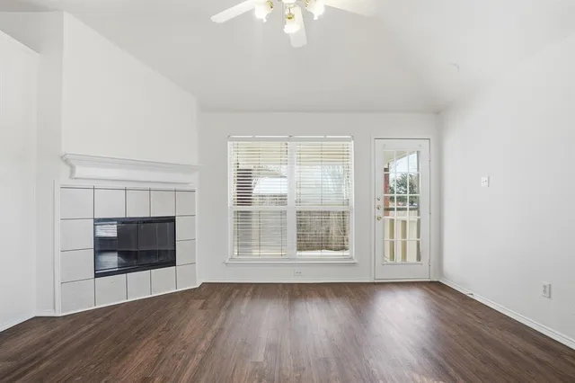 an empty room with wooden floor fire place and windows