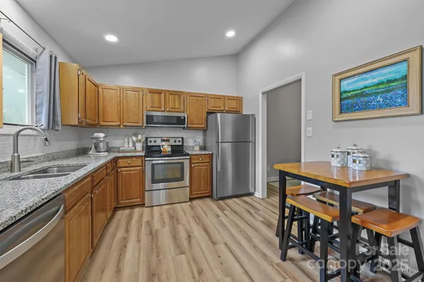 a kitchen with stainless steel appliances granite countertop a refrigerator a sink dishwasher a stove with wooden cabinets and floor