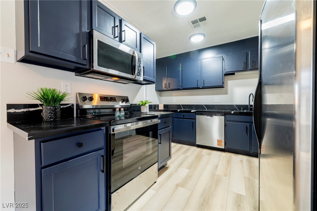 238 Kansas Avenue Henderson, NV 89015 - Photo 12 of 61 Kitchen with dark countertops, appliances with stainless steel finishes, blue cabinetry, and light wood-style floors
