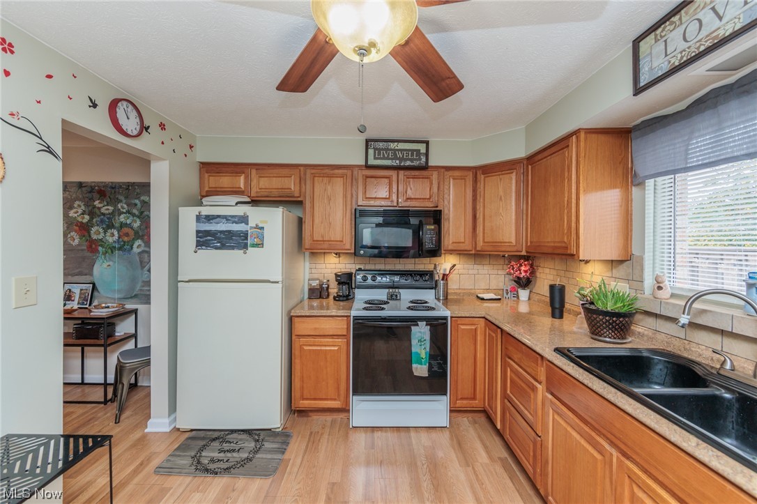 6476 State Road, Unit H8 Cleveland, OH 44134 - Photo 12 of 35 Kitchen featuring white refrigerator, backsplash, brown cabinets, light hardwood flooring, range with electric cooktop, and ceiling fan