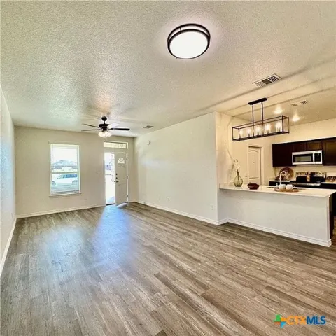 an empty room with wooden floor kitchen view and windows