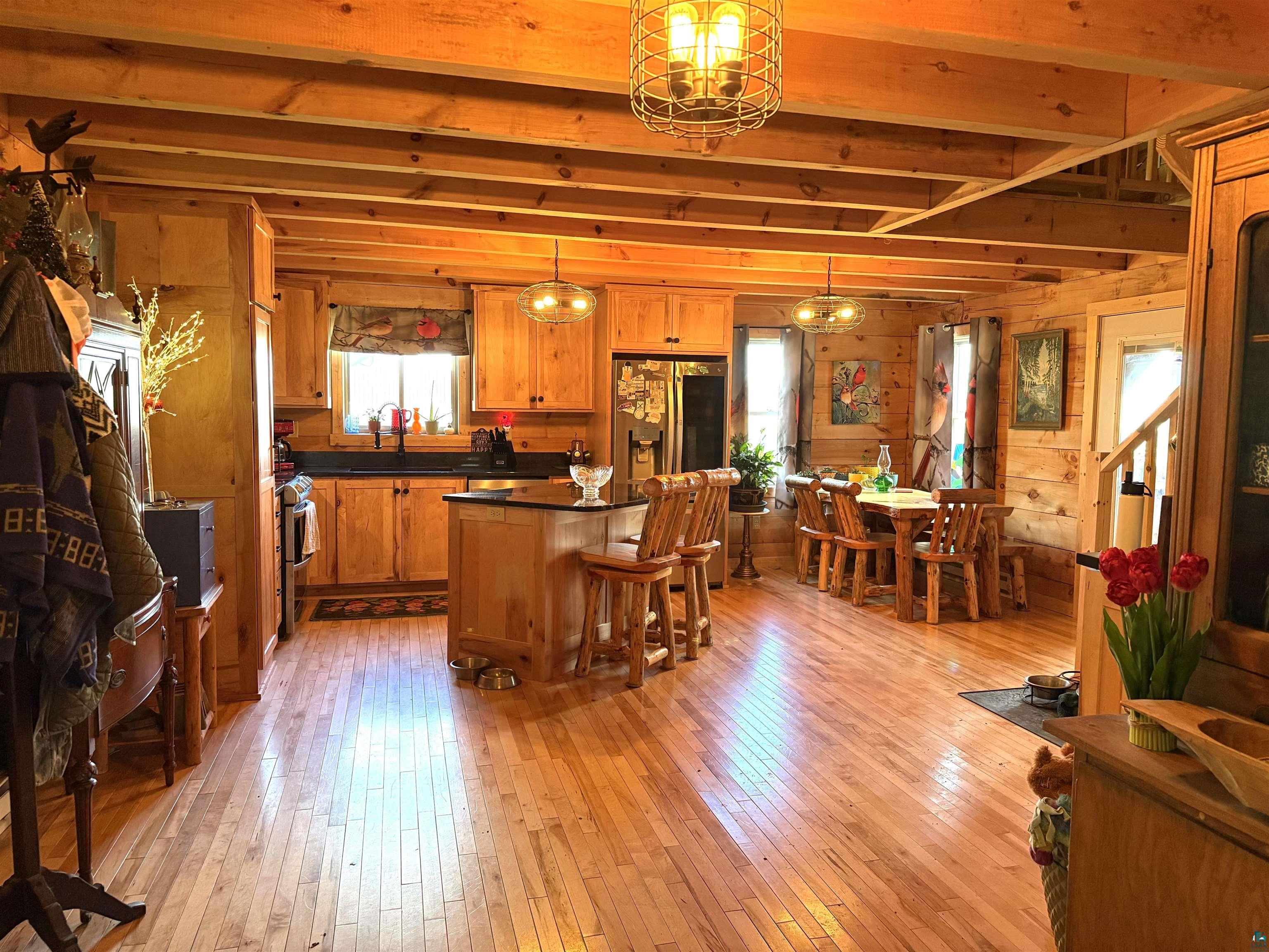37590 Degerstrom Road Askov, MN 55704 - Photo 9 of 53 Open-concept living space featuring exposed wood beam ceilings, light wood-finish flooring, and natural wood panel walls