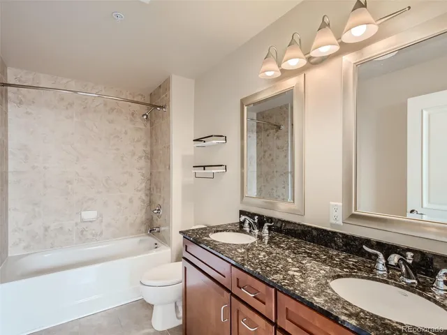 a bathroom with a granite countertop sink a toilet a mirror a bathtub and shower