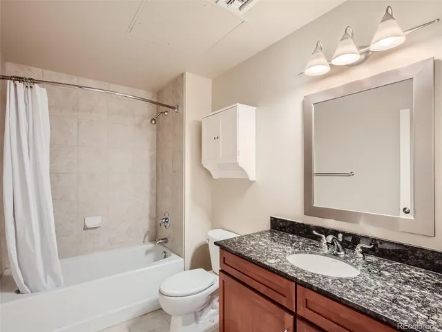 a bathroom with a granite countertop sink a toilet a mirror a vanity and shower