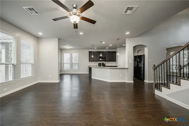 an empty room with wooden floor a ceiling fan and kitchen view