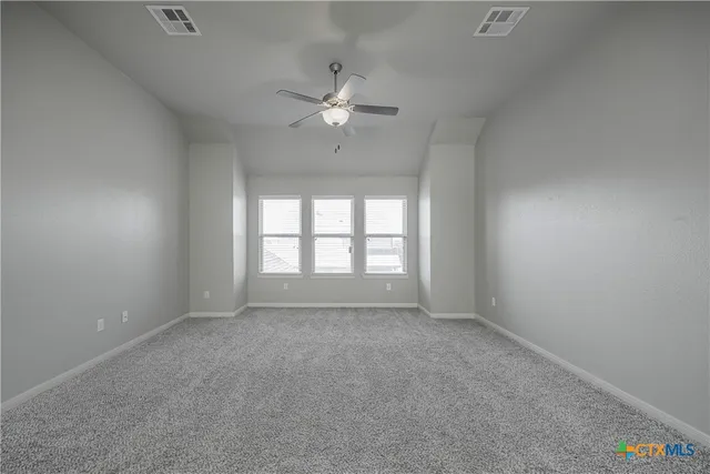 an empty room with chandelier fan and windows
