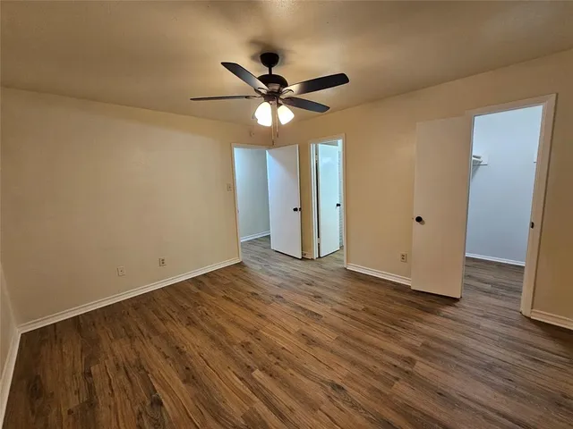 a view of an empty room with wooden floor and a ceiling fan