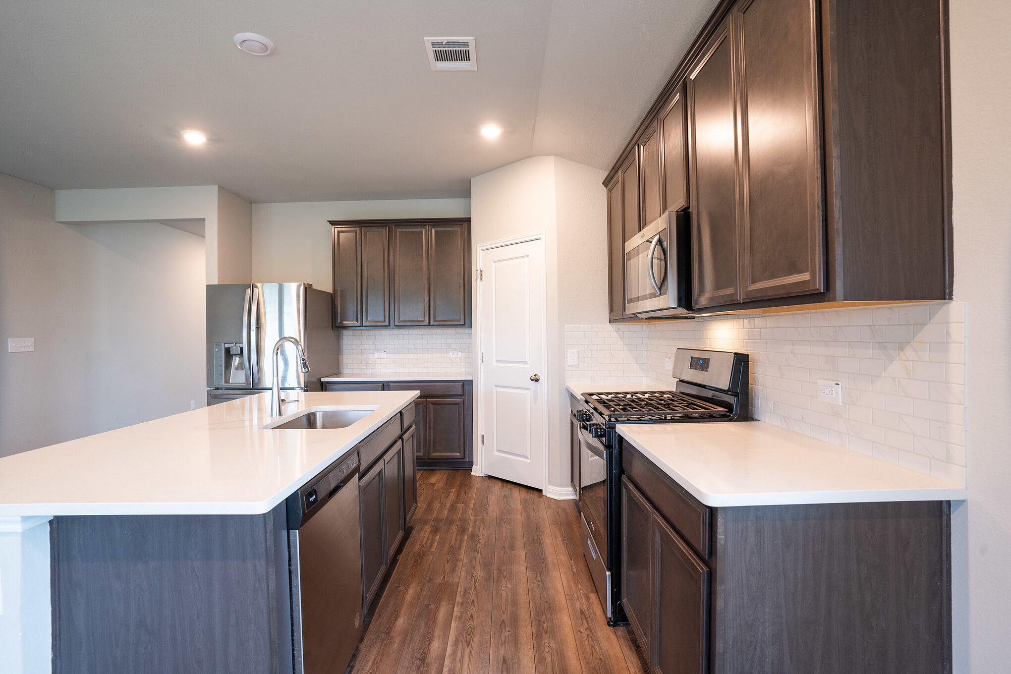 518 Windy Reed Road Hutto, TX 78634 - Photo 16 of 30 Spacious kitchen with stainless steel appliances, dark cabinets and an island with sink. The striking herringbone backsplash and EVP flooring with a warm wood-style feel make this area very inviting.