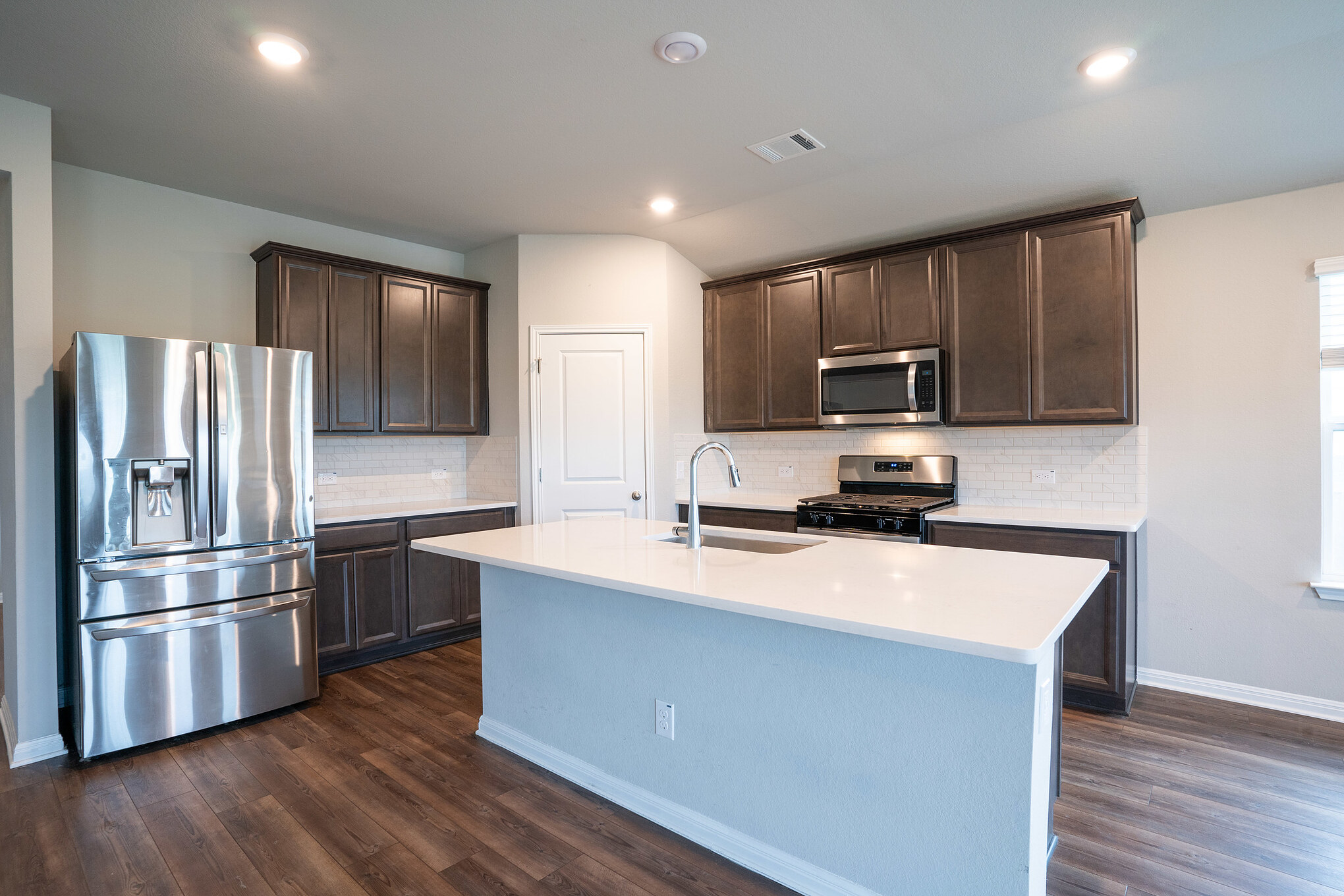 518 Windy Reed Road Hutto, TX 78634 - Photo 2 of 30 Spacious kitchen with stainless steel appliances, dark cabinets and an island with sink. The striking herringbone backsplash and EVP flooring with a warm wood-style feel make this area very inviting.